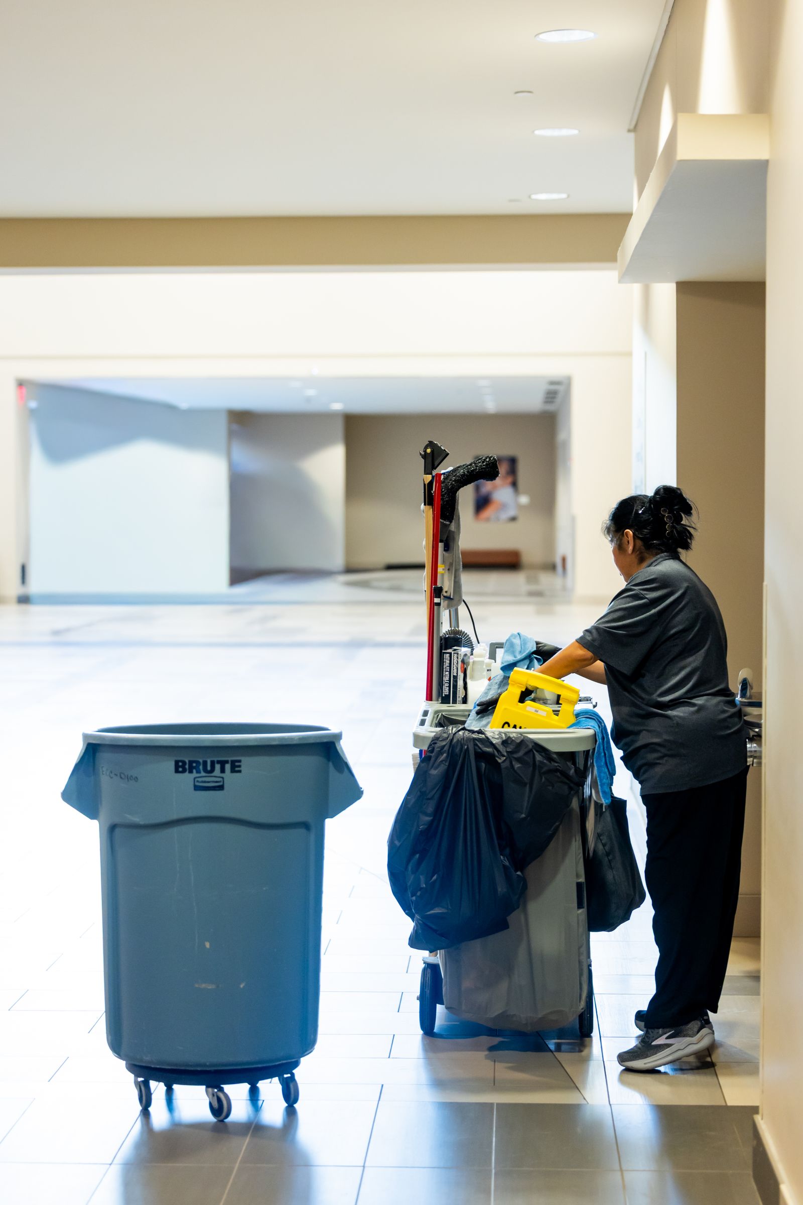 Janitorial worker pushing a cleaning cart in a spacious hallway